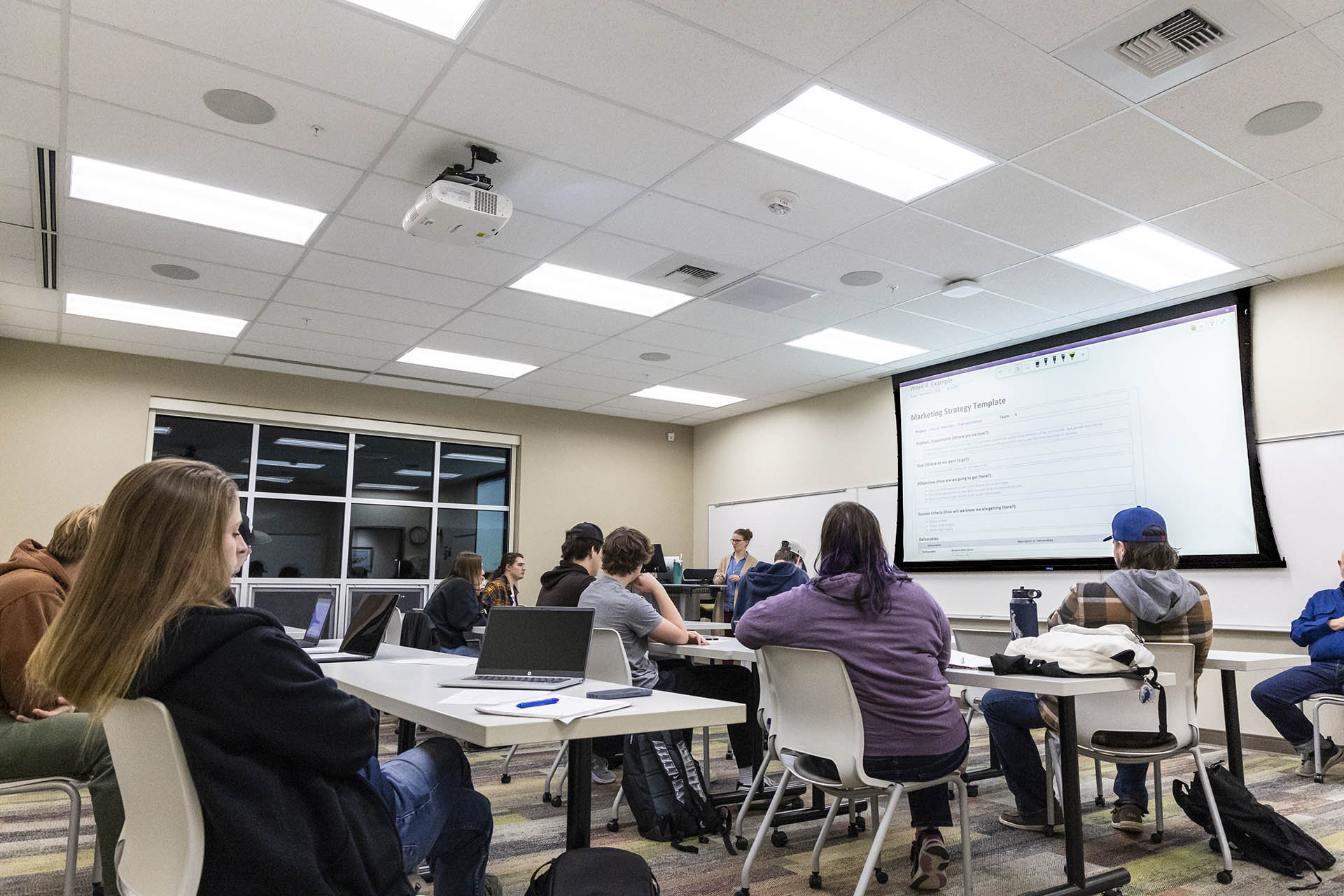 Business classroom full of students looking at a presentation on the board in front of them.