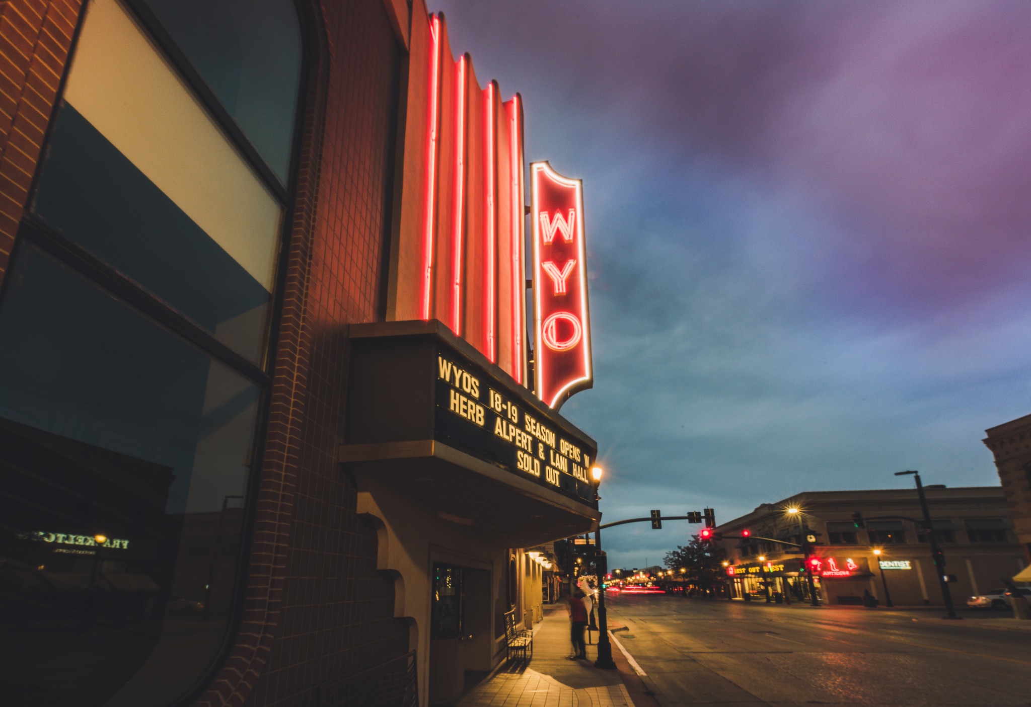 WYO Theater photo with the outside sign illuminated under a dark sunset sky and traffic lights of main street glowing