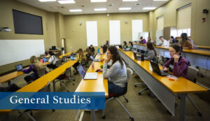 Photo of a tiered, brightly lit classroom with rows of students at their desks with laptops.