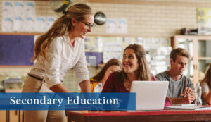 Photo of teacher working with a high school student who is at their desk with a laptop in a classroom.