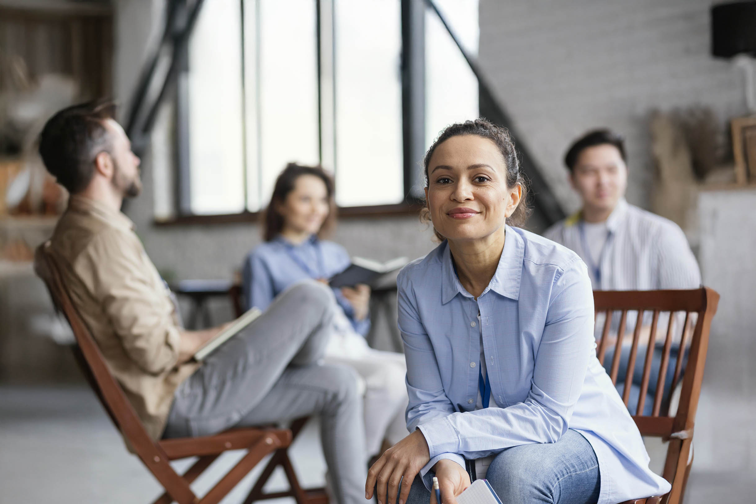Woman in a room smiling at the camera with others behind her in what appears to be a counseling session