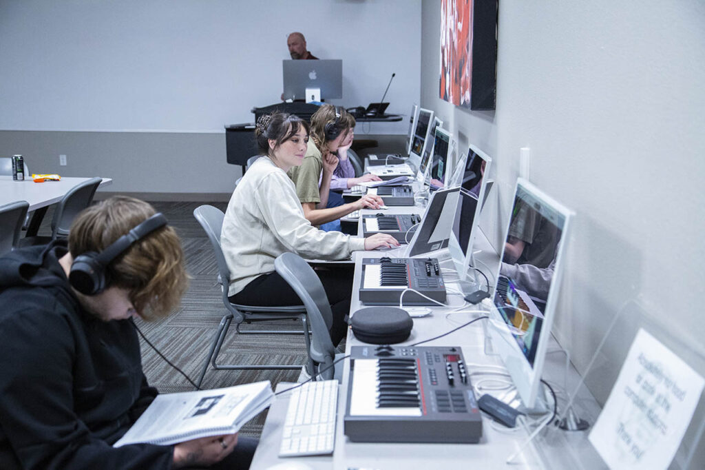 Students in the music tech lab with computers on the desk and MIDI keyboards as well