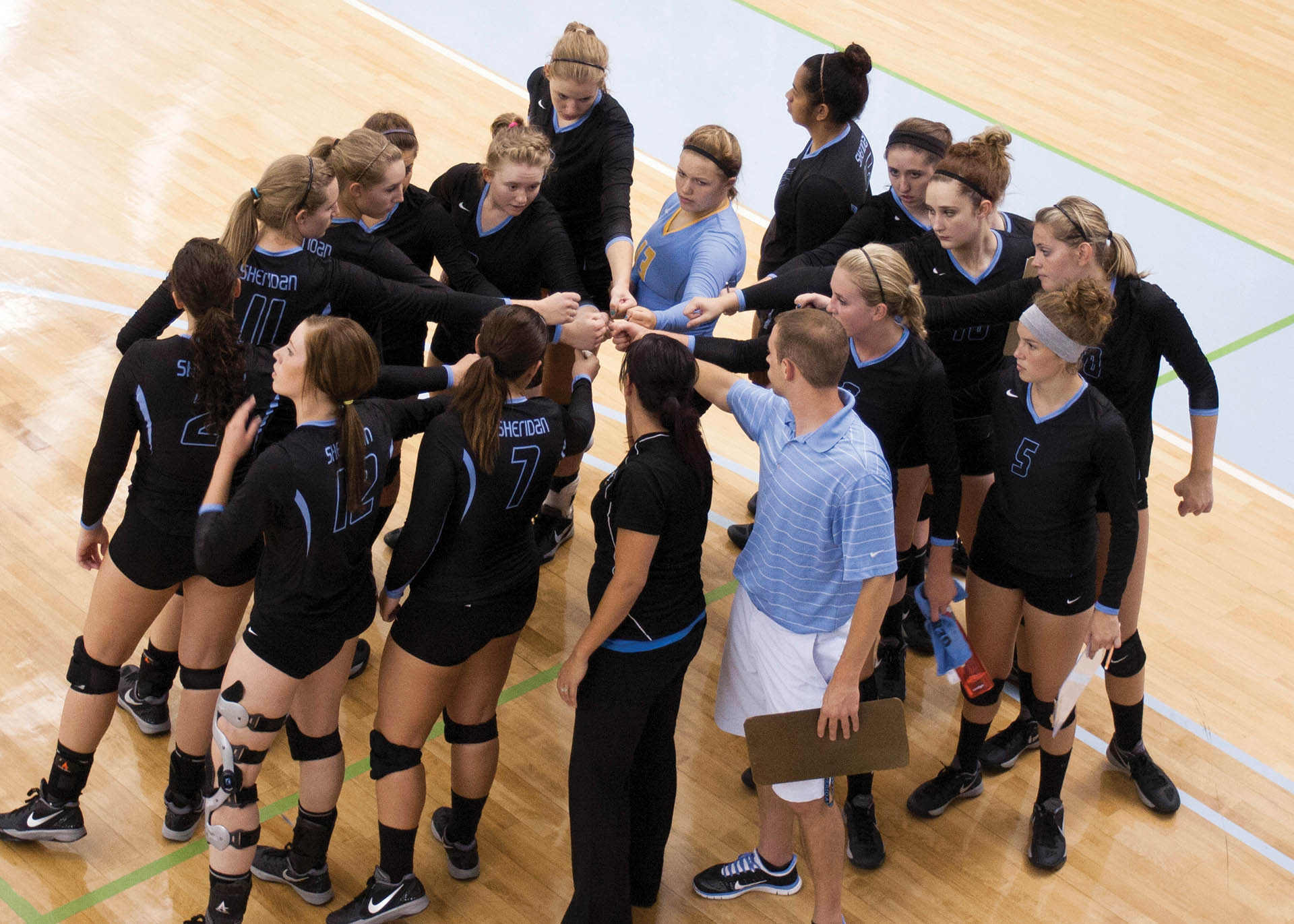Group of Sheridan volleyball athletes with their fists all in the center