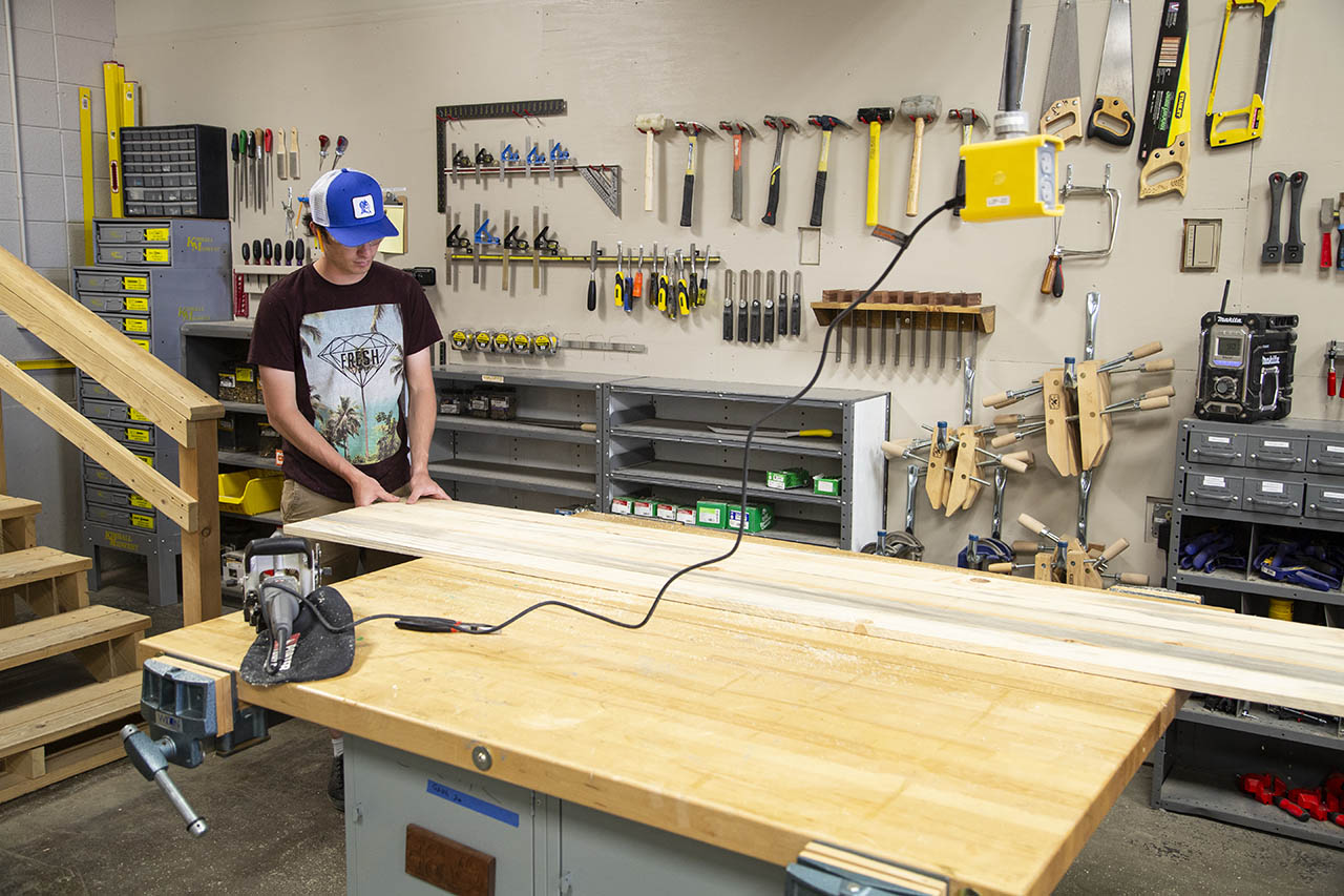 Student working at a big open table with a wall covered in construction tools behind them