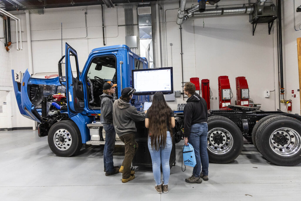 Students looking at a computer diagnostic screen hooked up to a diesel semi truck.