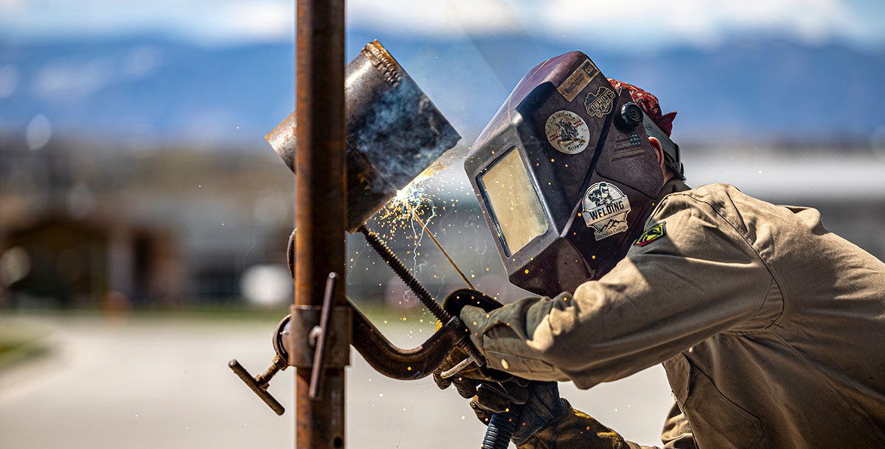 Welding student at Sheridan College with Bighorn Mountains in the background.