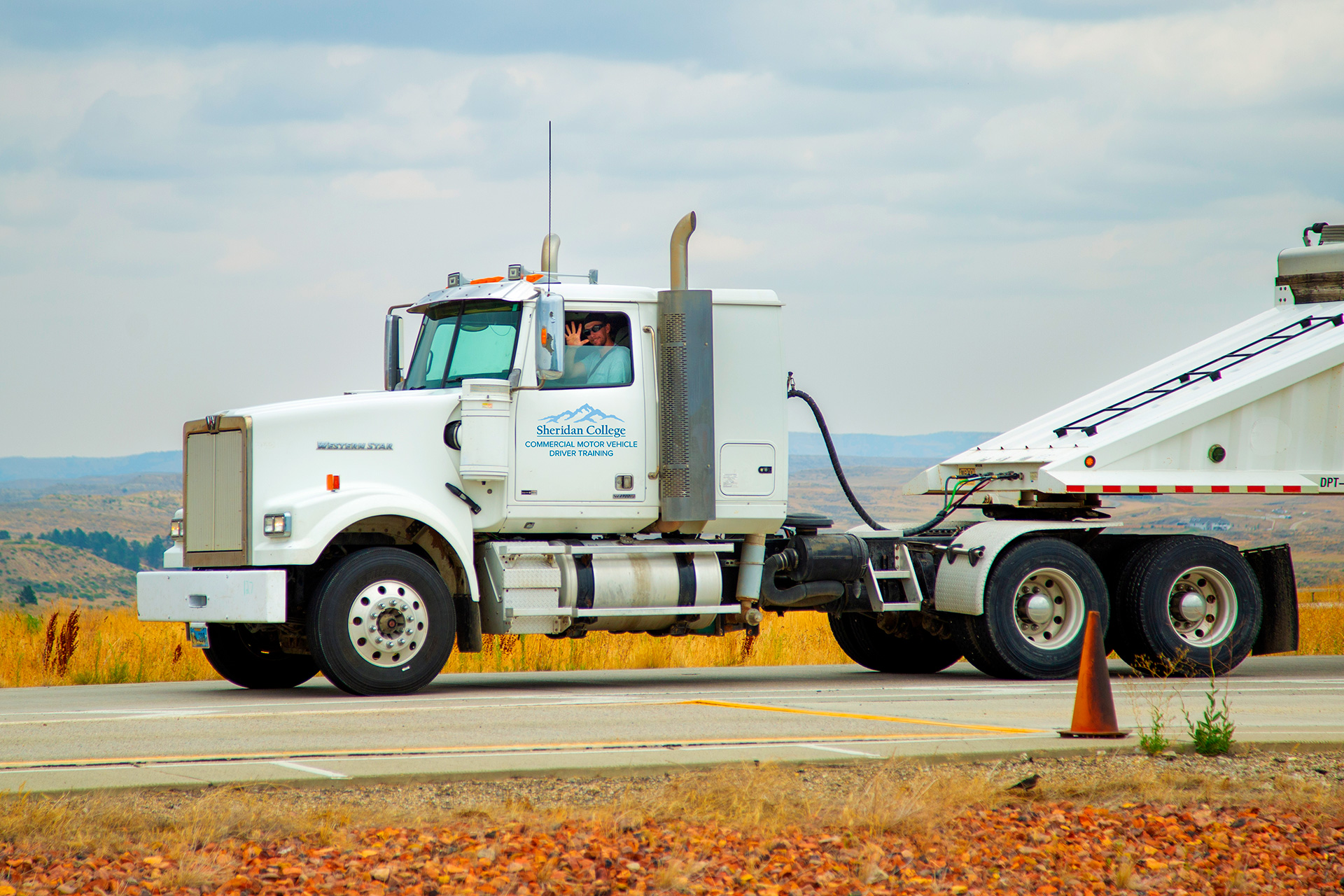 Sheridan College Commercial Motor Vehicle Driver Training program student waving from the window of a semi-truck.