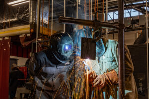 Sheridan College student welding while an instructor inspects in real-time.