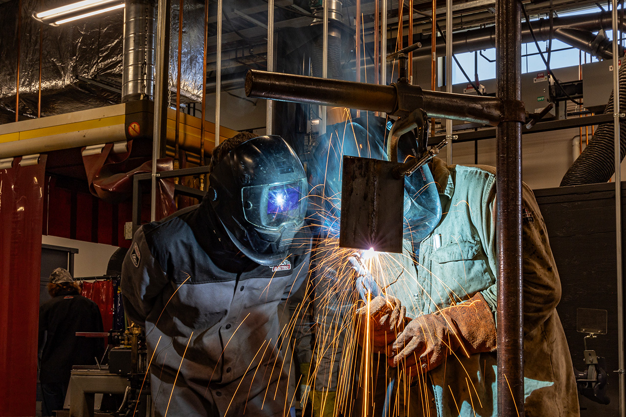 Sheridan College student welding while an instructor inspects in real-time.