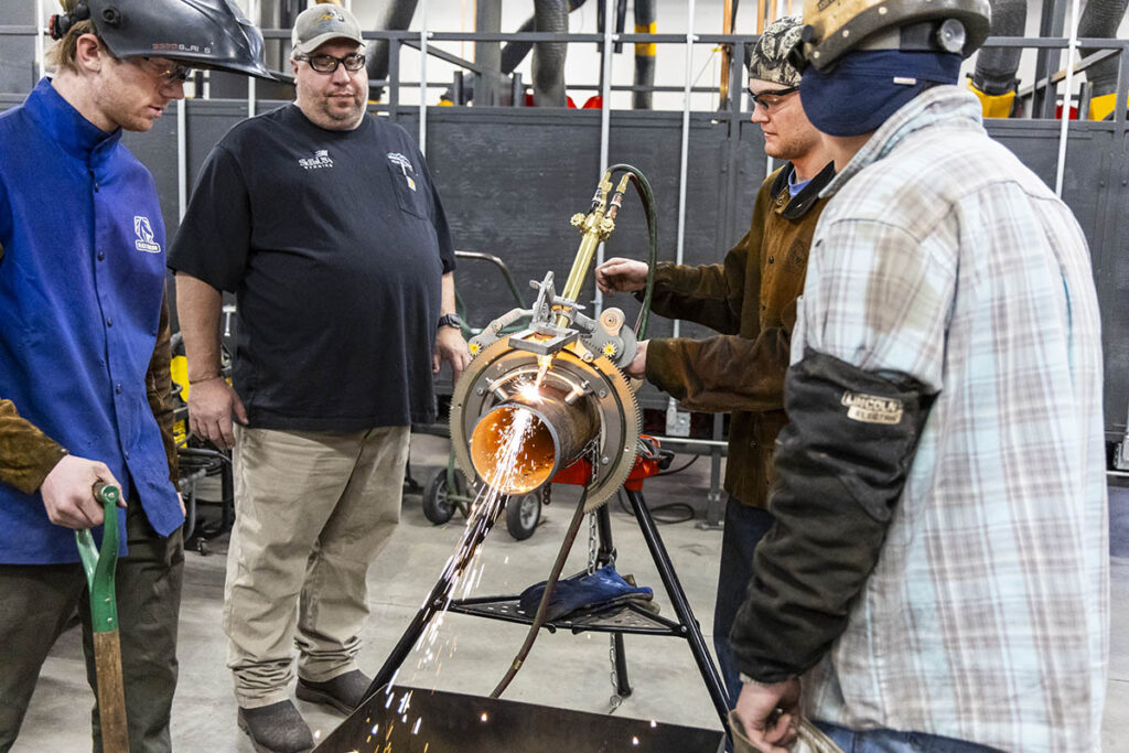 Students and faculty member using a torch cutter for cutting pipe