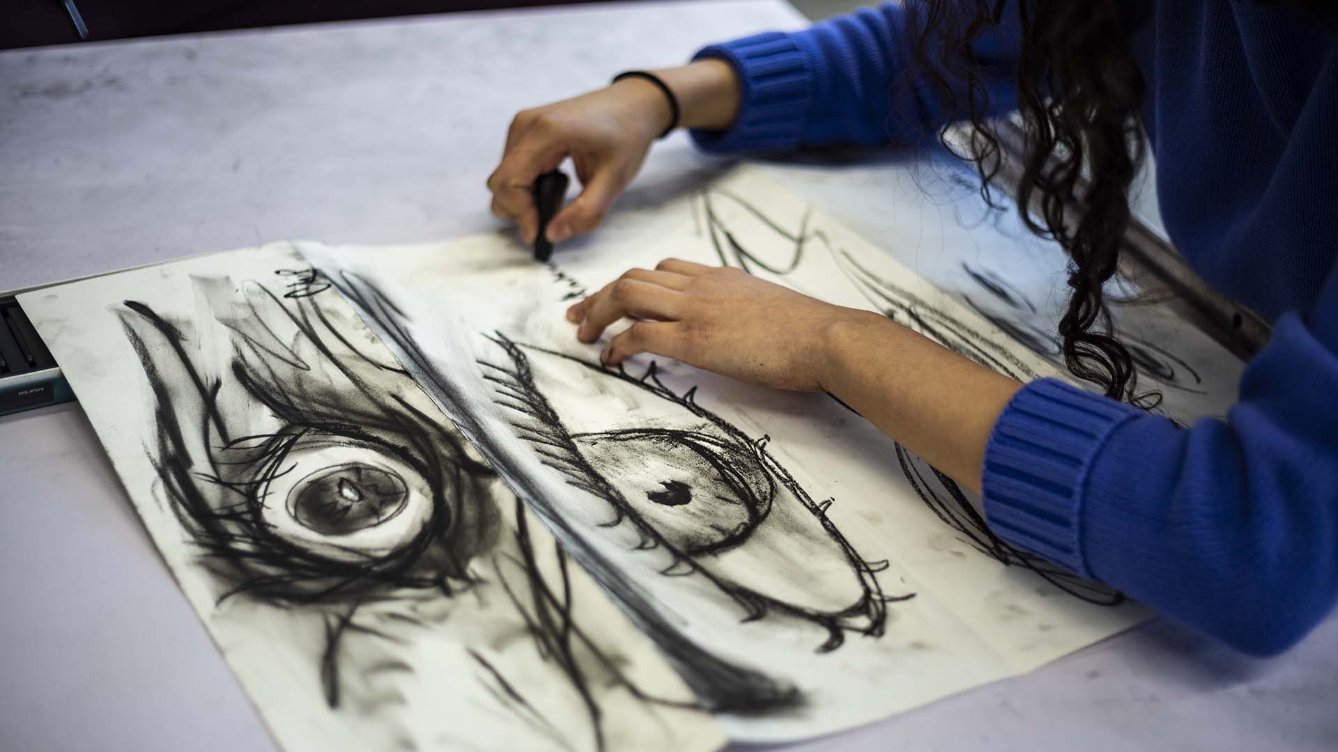 Student drawing with charcoal three different big eyeballs
