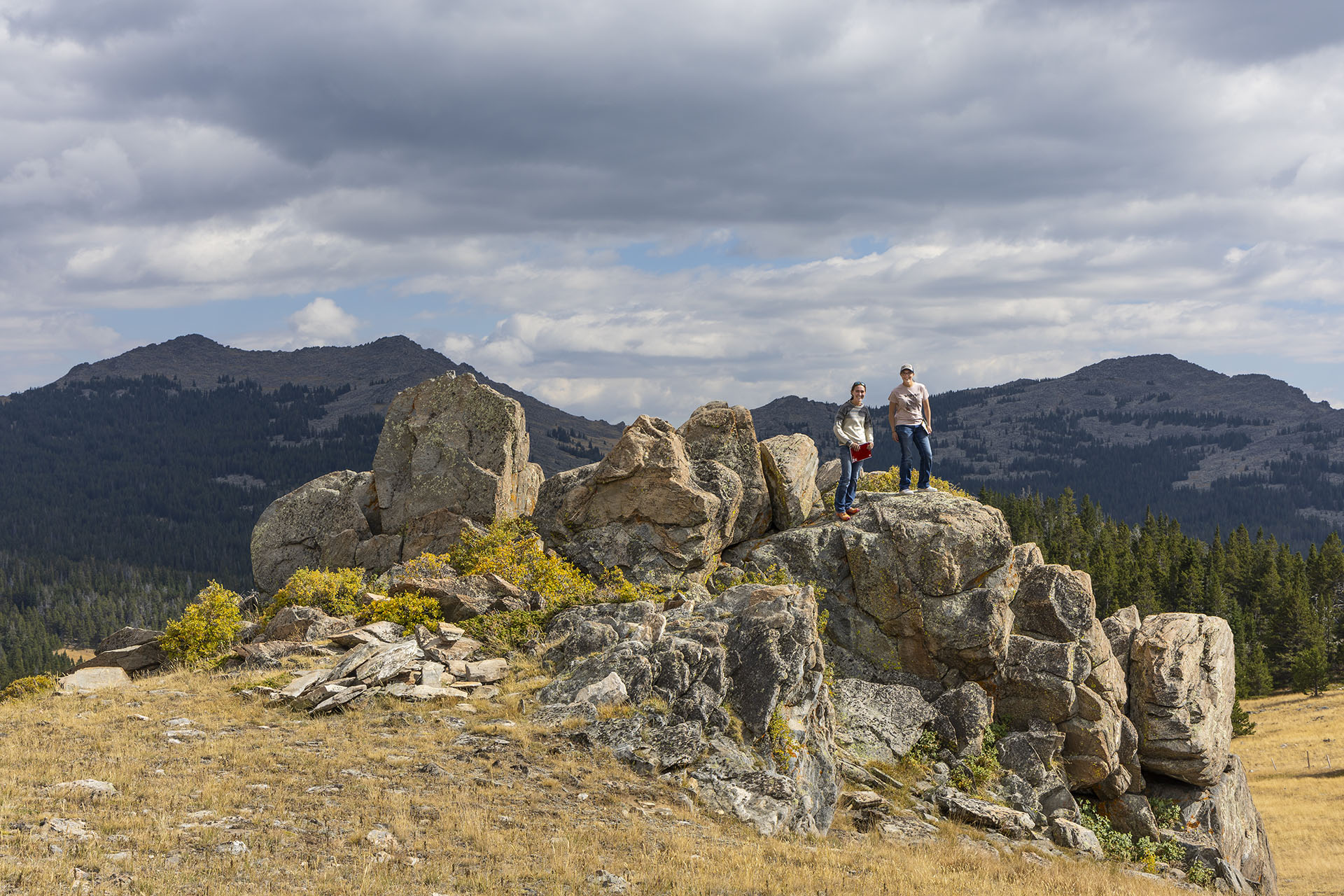 Two Sheridan College students standing on a rocky outcrop with 11,000 foot peaks behind them on Powder River Pass on a field trip