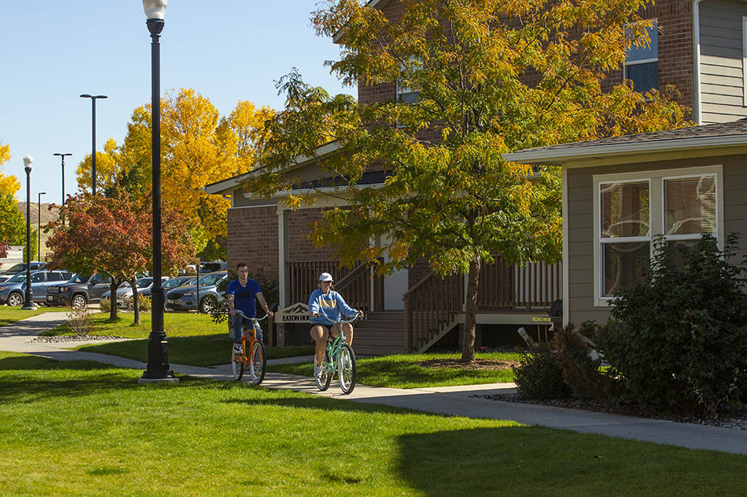 Students biking past on campus housing with fall colors in the trees