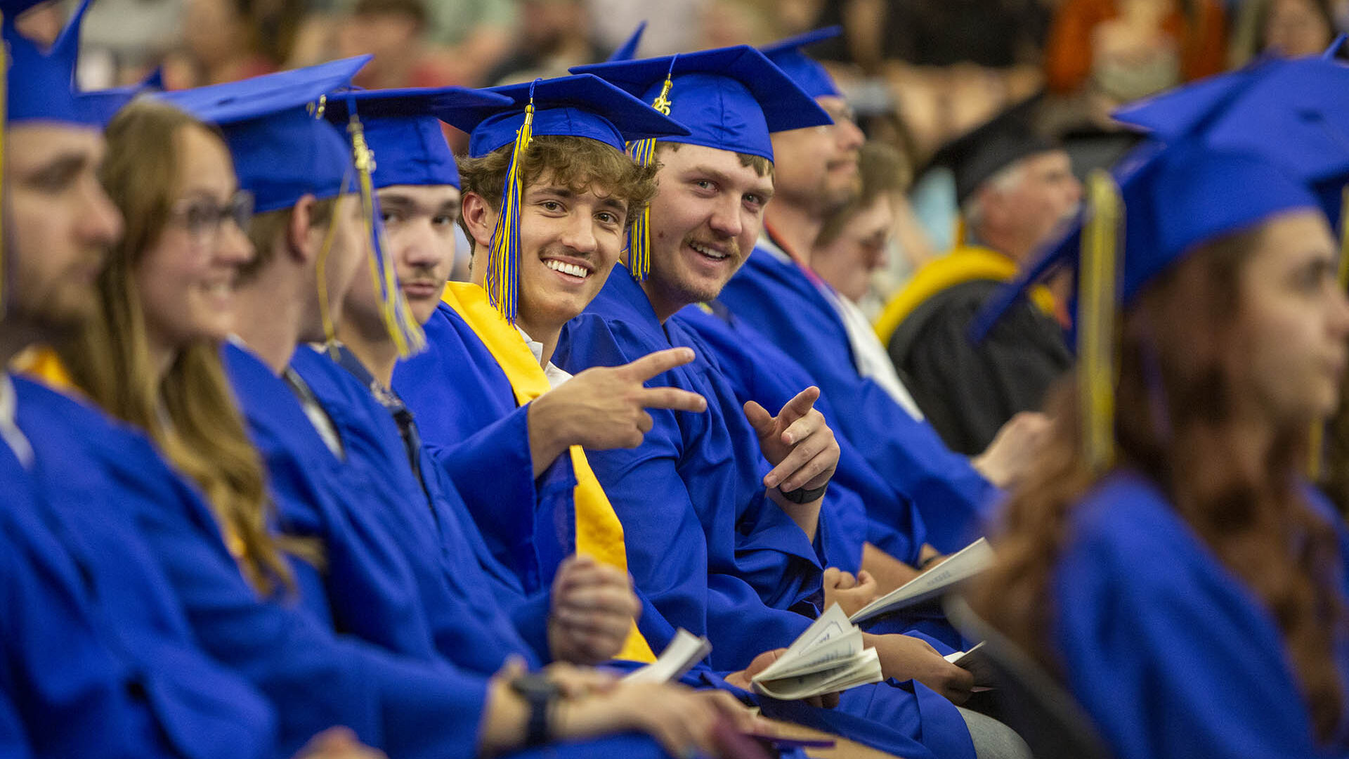 Photo of students smiling at graduation, looking at the camera and flashing a peace/victory sign