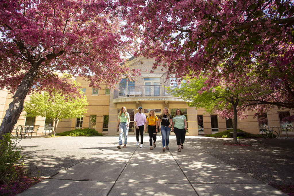 Founders Hall with trees blooming and students walking
