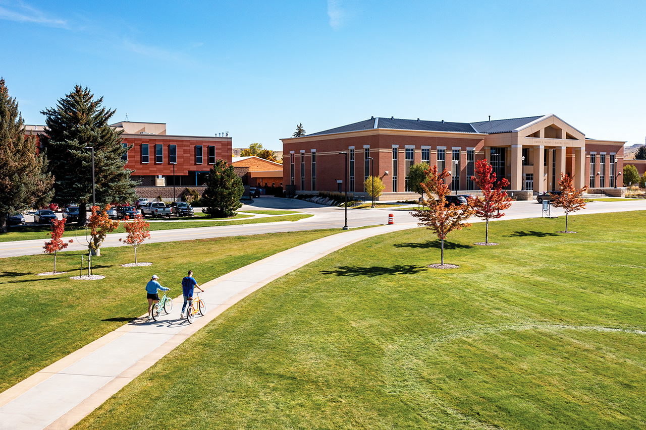 Sheridan College campus with students walking their bikes on pathway to the Whitney Academic Center.