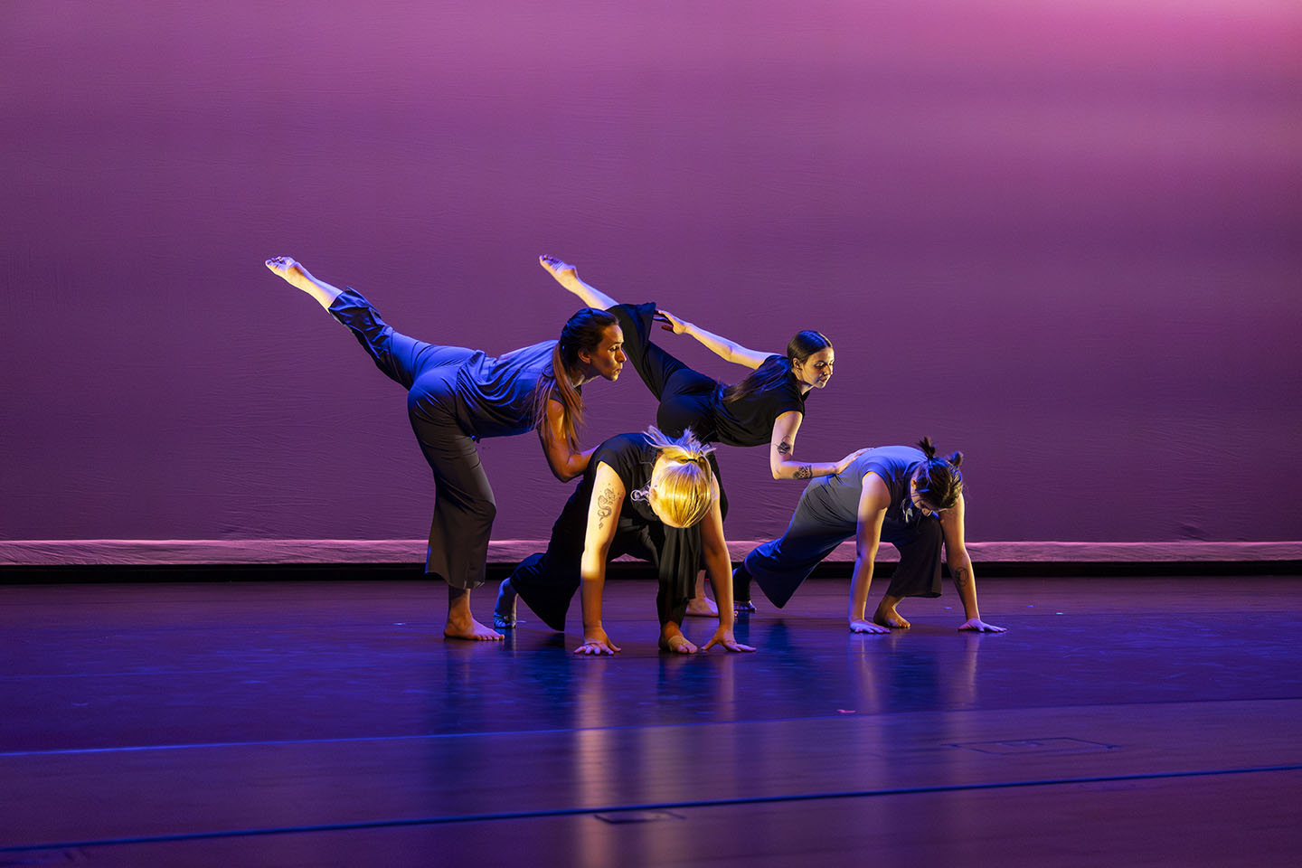 Two identically positioned dancers with their hands on the backs of two other bent dancers