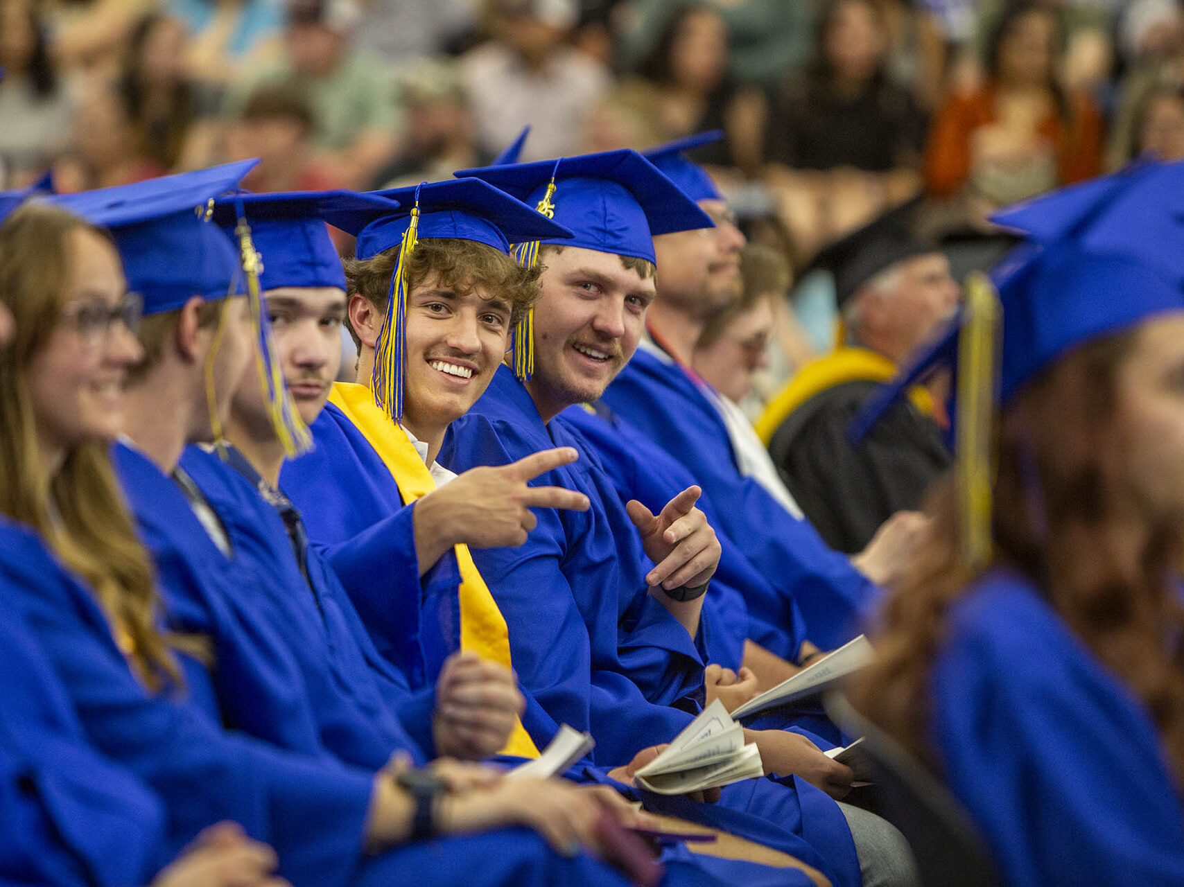 Photo of students smiling at graduation, looking at the camera and flashing a peace/victory sign