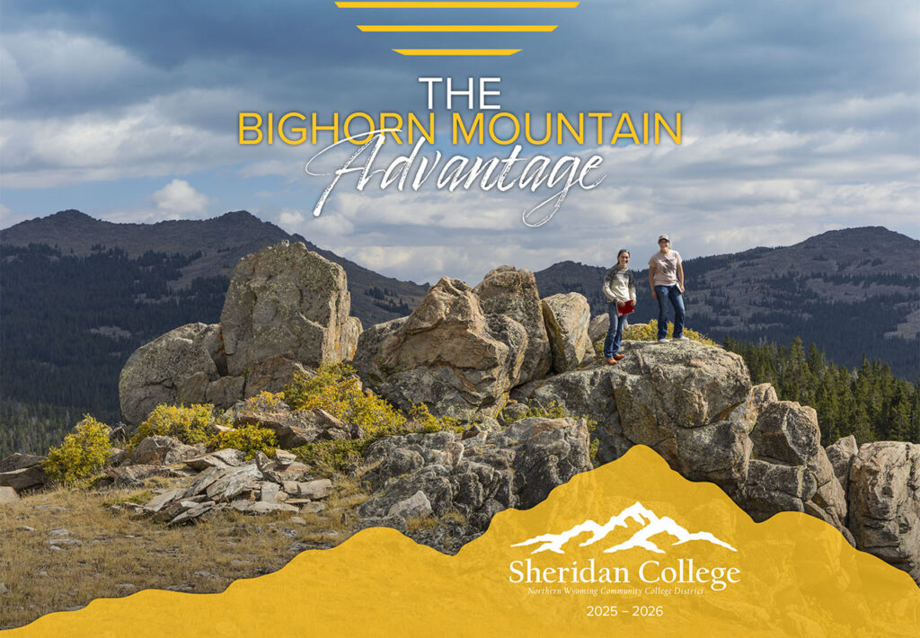 Two Sheridan College students standing on top of a rocky outcrop with alpine peaks in the background