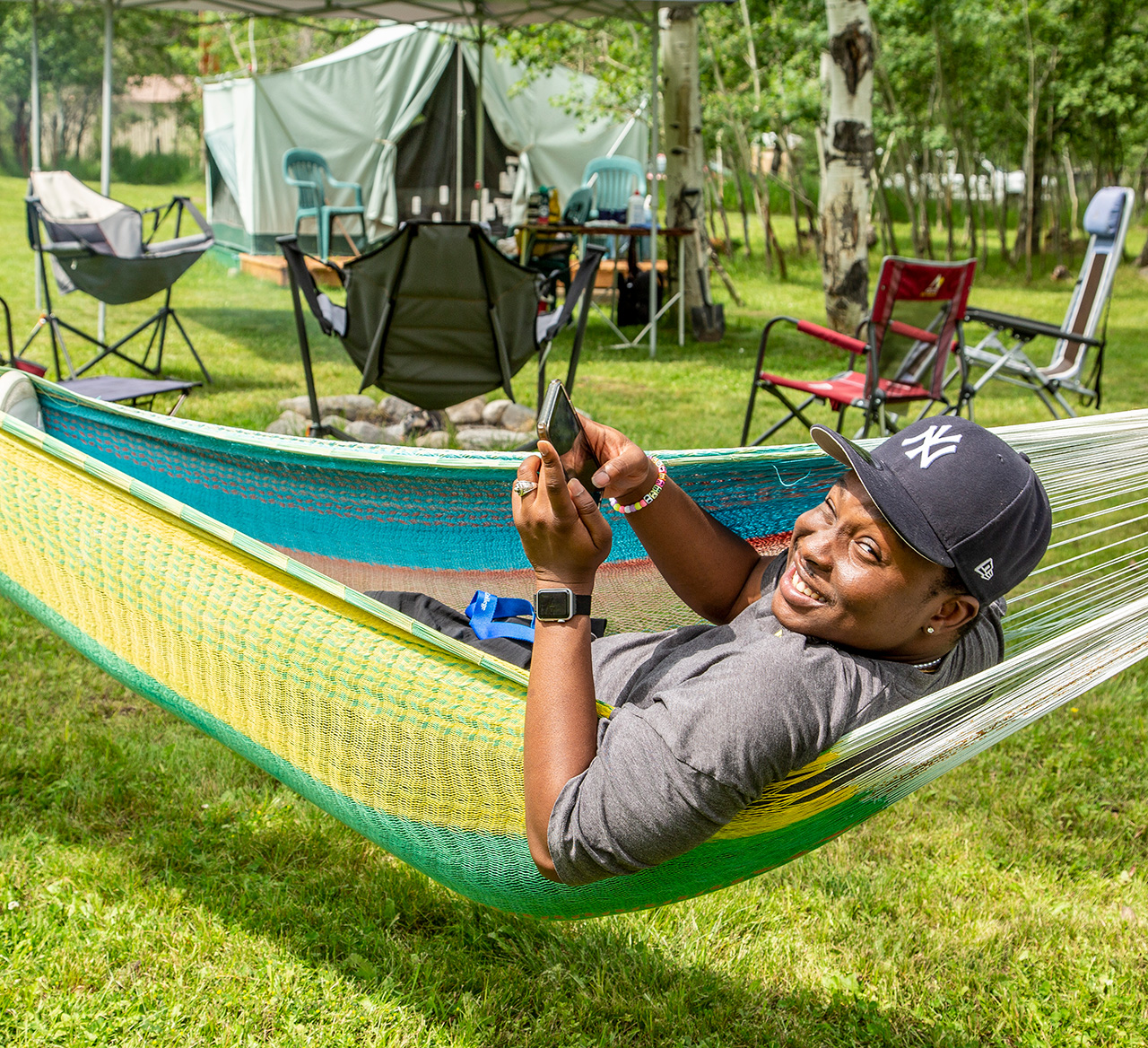 Sheridan College student looking at his phone while on a hammock.