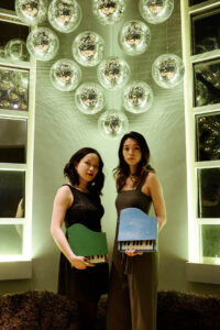 Photo of Chromic Duo standing in a unique room holding toy pianos