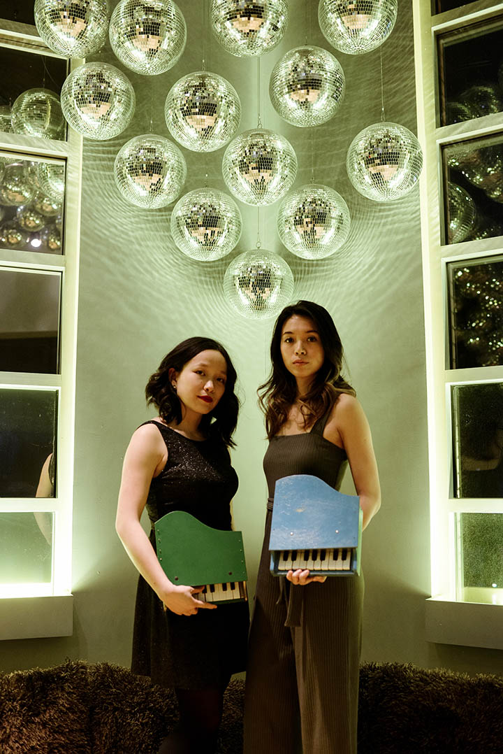 Photo of Chromic Duo standing in a unique room holding toy pianos