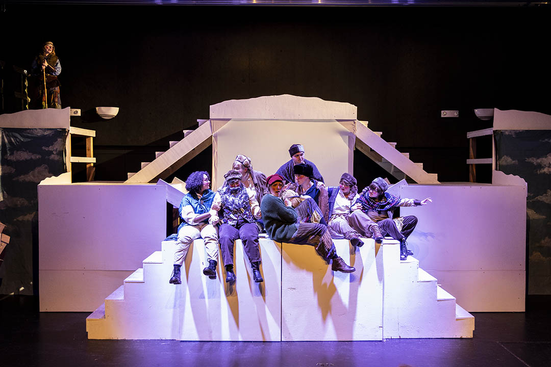 Actors on a theater set, crowded together and sitting at the top of some stairs during a production of The Snow