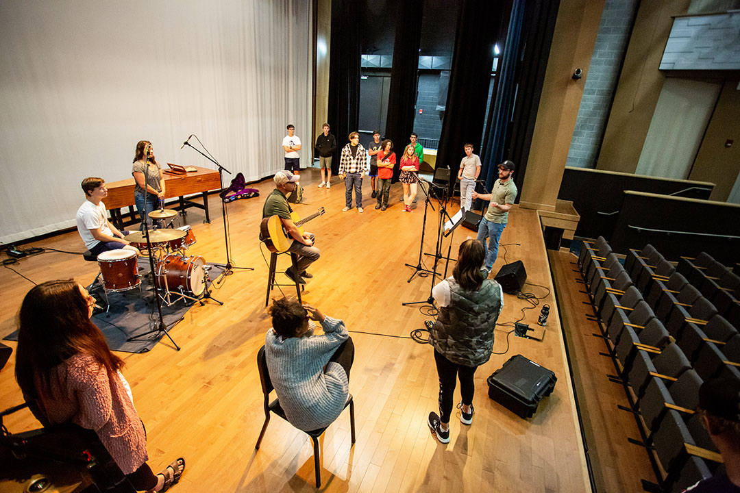 Music tech Camp students on stage in Kinnison Hall with a drum kit and acoustic guitar learning about live sound