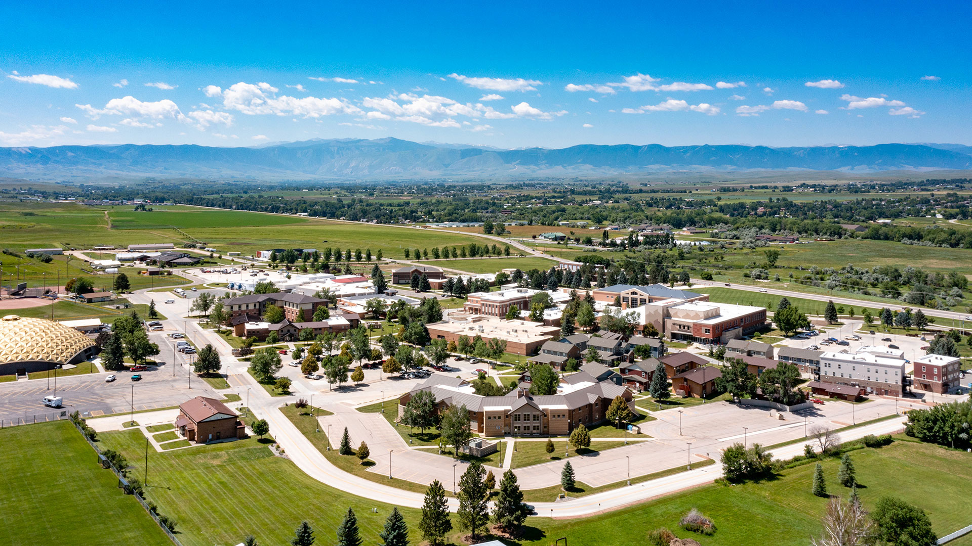 Drone image of Sheridan College campus with mountains in the background and blue skies.