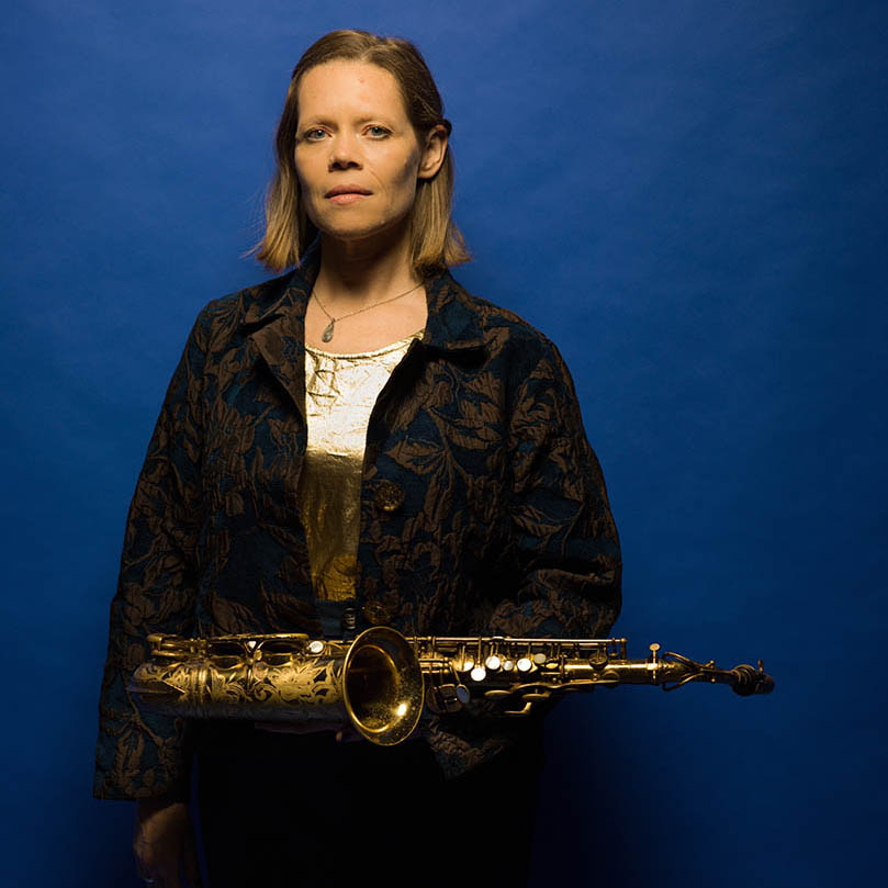 Photo of Caroline Davis with her saxophone against a blue background.